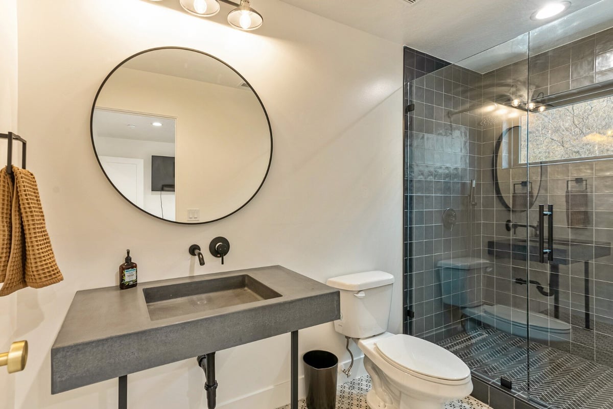 Attached Guest Bathroom with Gray Sink, Circular Mirror, Toilet and Large Walk-in Shower in Bear Lake Custom Home by 10X Builders