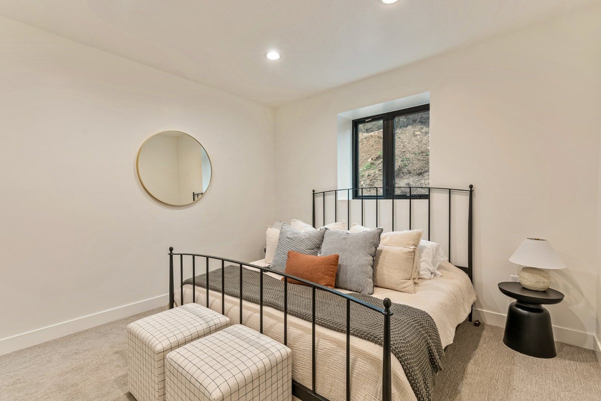 Bedroom with Metal Bed Frame Bed Under Window, Nightstand and Circular Mirror in Bear Lake Custom Home by 10X Builders