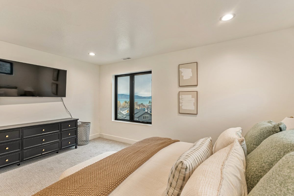 Neutral Bedroom with Window on Wall Next to Mounted Television and Dresser in Bear Lake Custom Home by 10X Builders