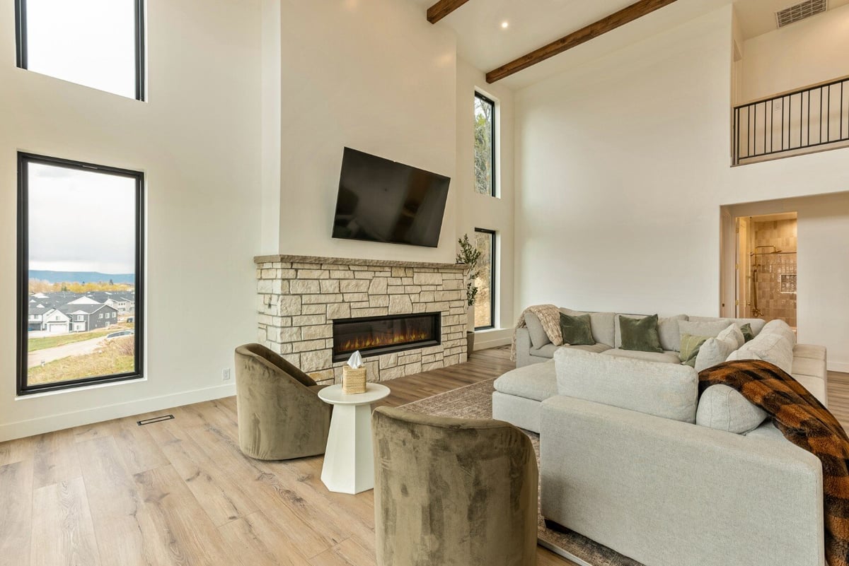 Side View of Living Room with Large Windows, Fireplace, Sectional, and View of Attached Bathroom and Above Catwalk in Bear Lake Custom Home by 10X Builders