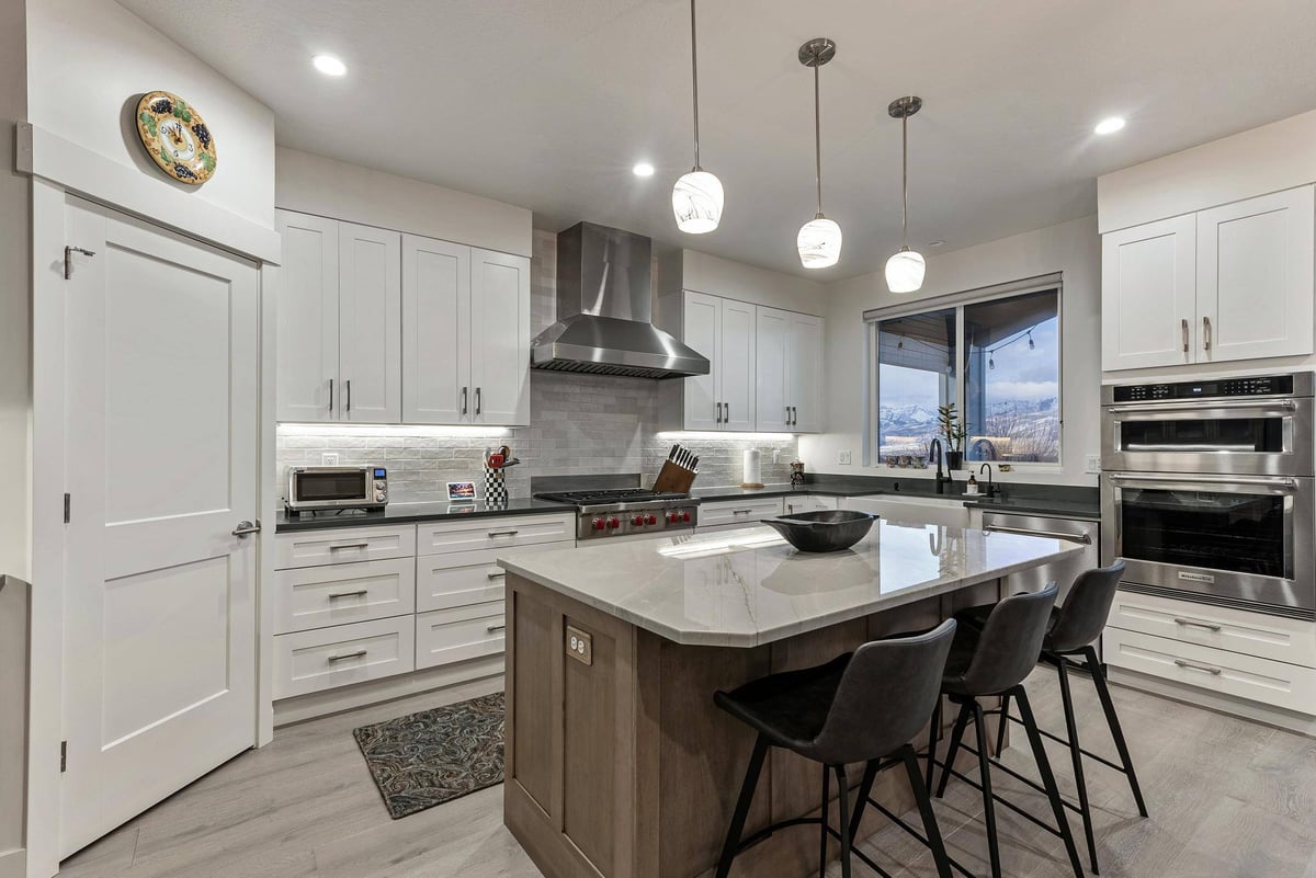 Kitchen Area Featuring an Island with Barstools, Two-Door Oven, Stovetop, and White Cabinetry in Remodeled Utah Home